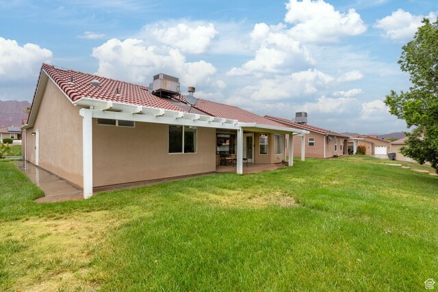 back of house featuring a tiled roof, a lawn, a patio area, stucco siding, and central AC unit