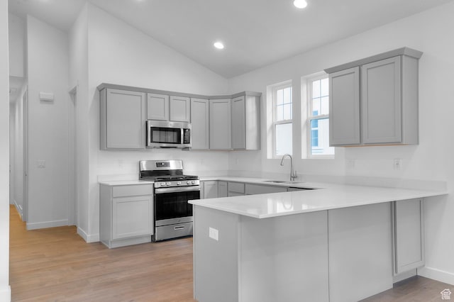kitchen featuring appliances with stainless steel finishes, gray cabinets, a sink, a peninsula, and lofted ceiling