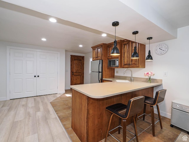 kitchen with stainless steel microwave, freestanding refrigerator, a sink, baseboards, and a kitchen breakfast bar