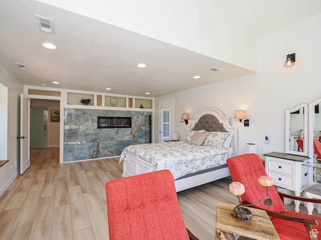 bedroom featuring recessed lighting, light wood-type flooring, and a glass covered fireplace