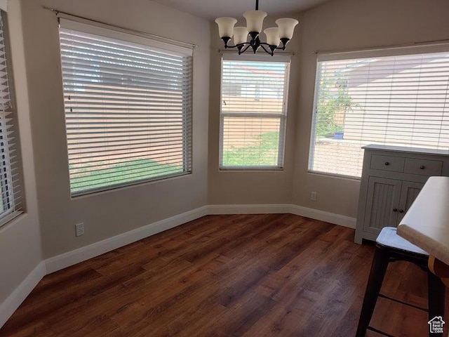 unfurnished dining area featuring dark wood-style flooring, a chandelier, and baseboards