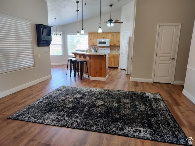 kitchen with white microwave, lofted ceiling, light brown cabinetry, ceiling fan, and baseboards