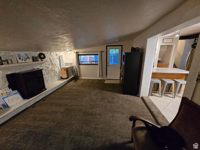 tiled living area with lofted ceiling, a textured ceiling, a stone fireplace, and carpet