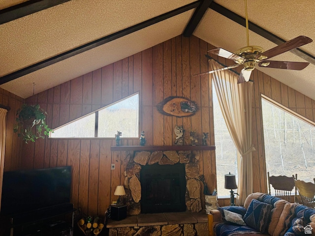 living room featuring wooden walls, ceiling fan, and a stone fireplace
