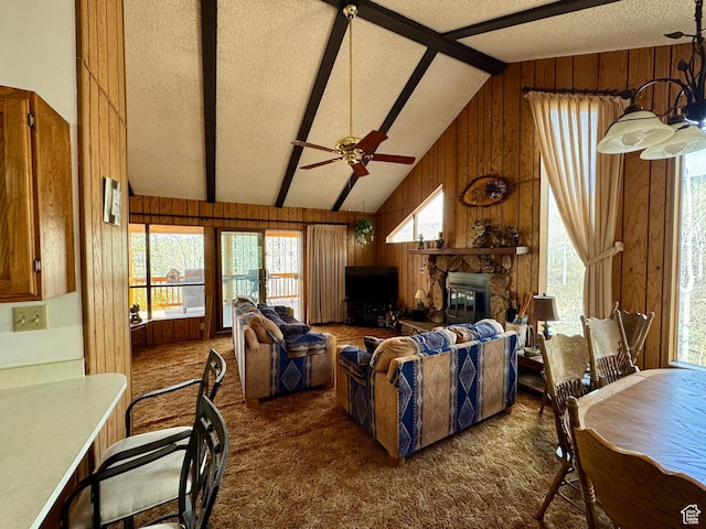 living area with wooden walls, dark colored carpet, a ceiling fan, a stone fireplace, and a textured ceiling