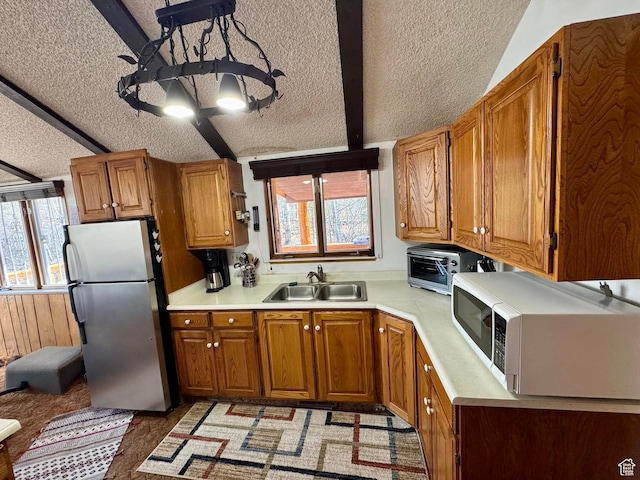 kitchen featuring freestanding refrigerator, a sink, white microwave, a textured ceiling, and brown cabinetry