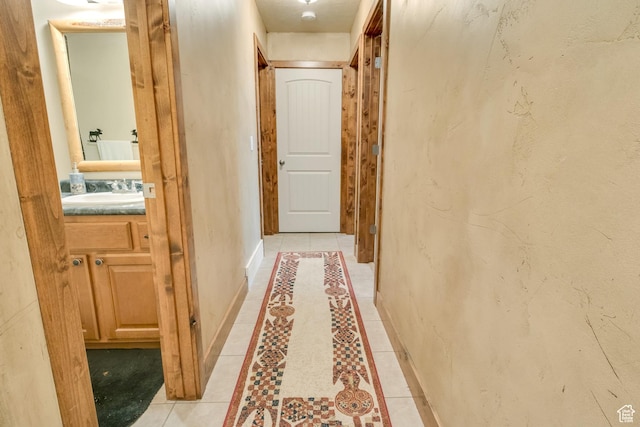 corridor with a sink, baseboards, inlaid floor details, and light tile patterned flooring