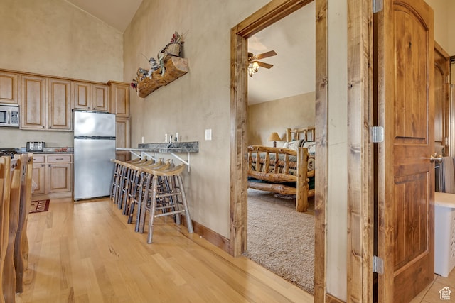 kitchen with appliances with stainless steel finishes, light wood finished floors, high vaulted ceiling, a ceiling fan, and dark countertops