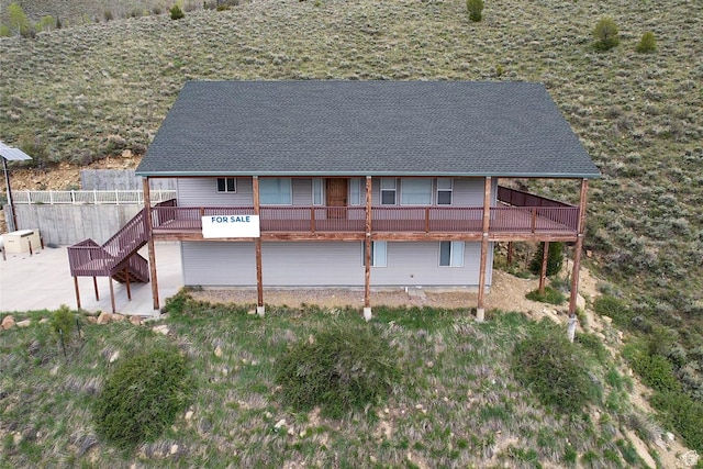 rear view of property with a patio area, roof with shingles, a deck, and stairway