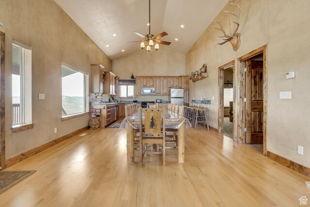 dining room featuring ceiling fan, light wood-type flooring, high vaulted ceiling, and baseboards