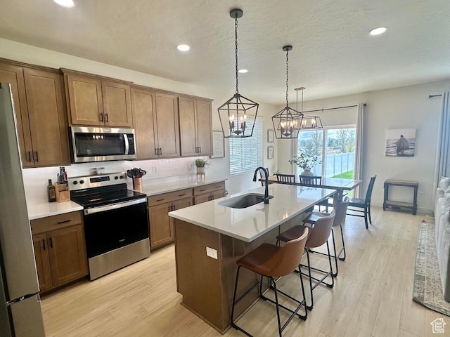 kitchen with stainless steel appliances, a sink, tasteful backsplash, a kitchen bar, and light wood finished floors