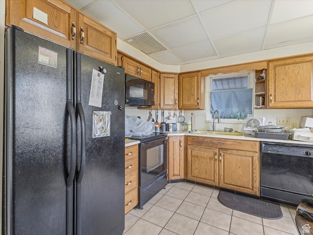 kitchen featuring black appliances, a sink, light tile patterned floors, light countertops, and brown cabinetry