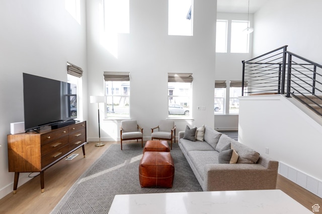 living area with a towering ceiling, wood finished floors, baseboards, and stairway