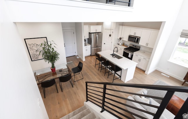 kitchen featuring appliances with stainless steel finishes, a sink, a kitchen breakfast bar, light wood-style flooring, and white cabinets