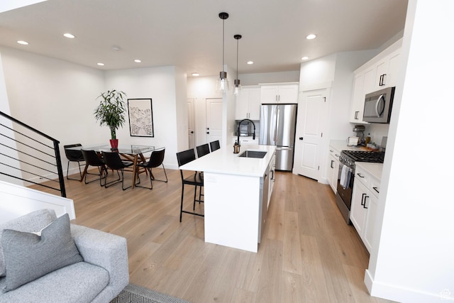 kitchen with stainless steel appliances, a sink, a breakfast bar, light wood-type flooring, and recessed lighting