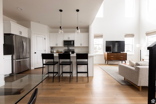 kitchen with appliances with stainless steel finishes, white cabinetry, light wood finished floors, a kitchen island with sink, and open floor plan