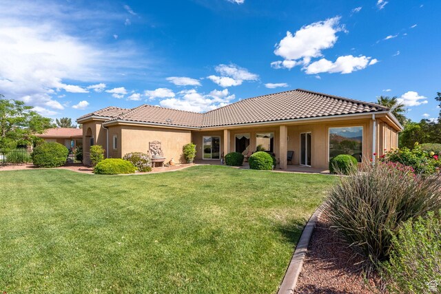back of property featuring a tile roof, stucco siding, and a lawn