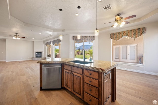 kitchen featuring a sink, stainless steel dishwasher, a ceiling fan, brown cabinets, and a textured ceiling