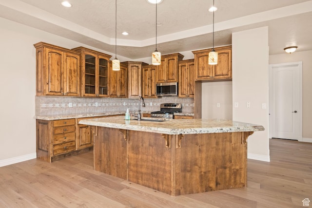 kitchen with stainless steel appliances, brown cabinets, baseboards, light wood finished floors, and light stone counters