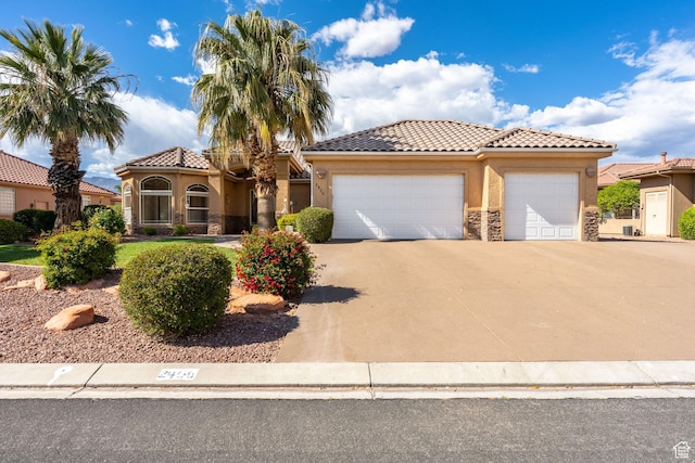 mediterranean / spanish house featuring driveway, a garage, stucco siding, stone siding, and a tile roof