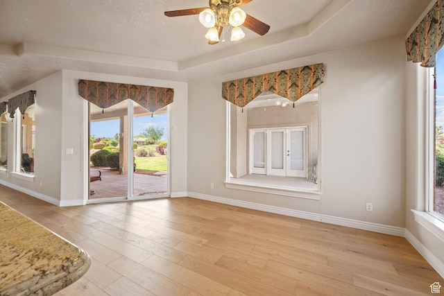 empty room featuring light wood-type flooring, a ceiling fan, baseboards, and a raised ceiling
