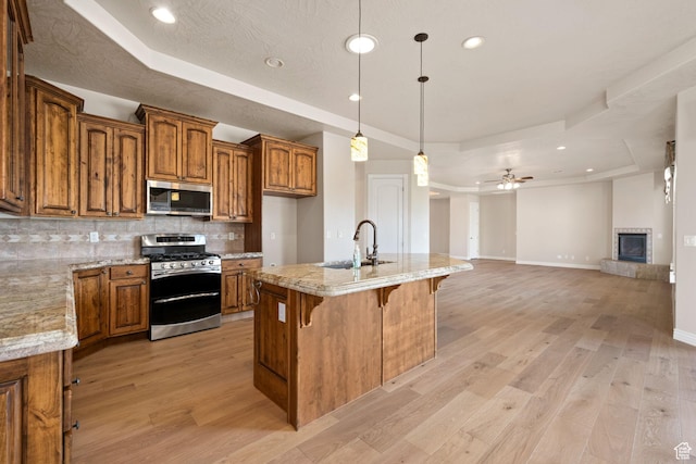 kitchen featuring stainless steel appliances, a tray ceiling, brown cabinets, a sink, and backsplash
