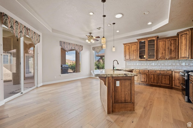 kitchen featuring a tray ceiling, a sink, double oven range, brown cabinetry, and recessed lighting