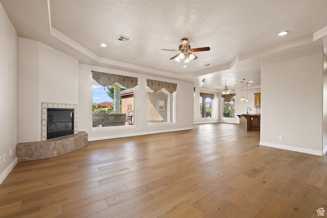unfurnished living room featuring a ceiling fan, a raised ceiling, light wood-style flooring, baseboards, and a high end fireplace