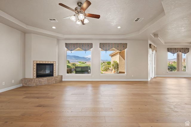 unfurnished living room featuring a raised ceiling, light wood-style flooring, a ceiling fan, a fireplace, and a textured ceiling