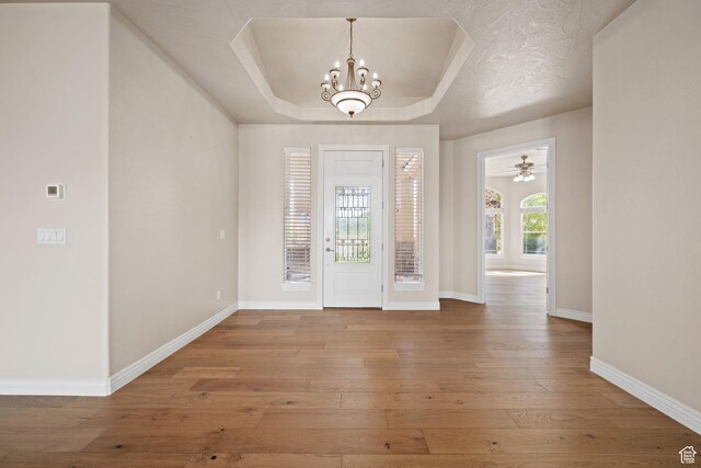 foyer with a tray ceiling, hardwood / wood-style floors, baseboards, and a chandelier
