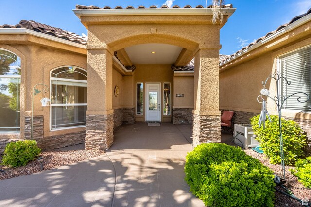 view of exterior entry with stone siding, stucco siding, and a tile roof