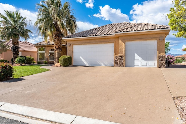mediterranean / spanish-style home with a tile roof, driveway, stucco siding, and stone siding