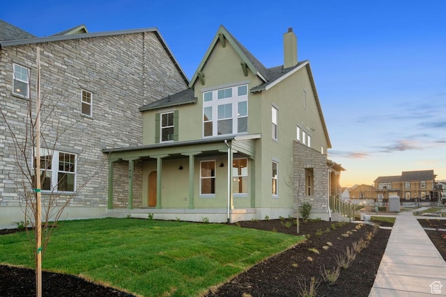 11419 S Watercourse Rd Unit 188, South Jordan, UT 84009 - back of house at dusk featuring stone siding, stucco siding, a porch, a chimney, and a lawn