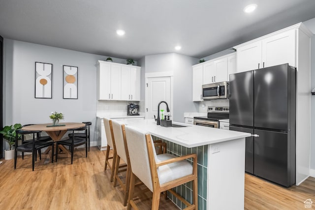 kitchen featuring stainless steel appliances, a sink, light wood-style flooring, decorative backsplash, and a kitchen island with sink
