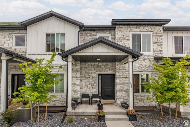 entrance to property with board and batten siding, stone siding, covered porch, and central AC unit