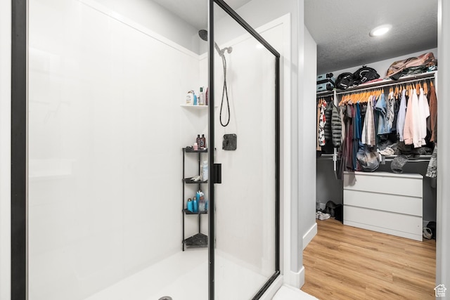 bathroom with a shower stall, a spacious closet, wood finished floors, and recessed lighting