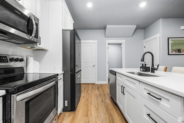 kitchen featuring stainless steel appliances, a sink, white cabinetry, light wood-style floors, and recessed lighting