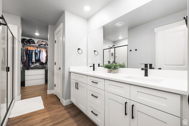 full bath featuring a shower stall, double vanity, a spacious closet, wood finished floors, and baseboards