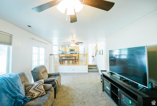 carpeted living room with a ceiling fan and stairs