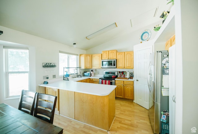 kitchen with appliances with stainless steel finishes, a peninsula, a sink, lofted ceiling, and light wood finished floors