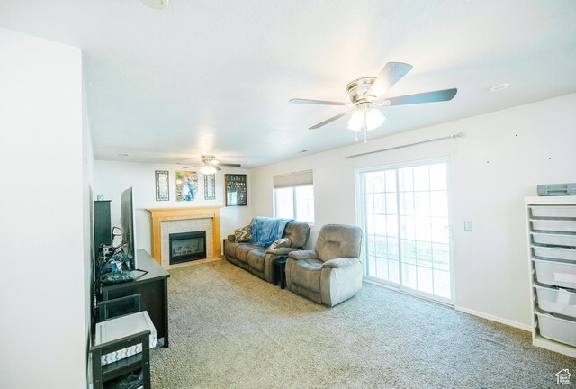 carpeted living area with ceiling fan, a tile fireplace, and baseboards