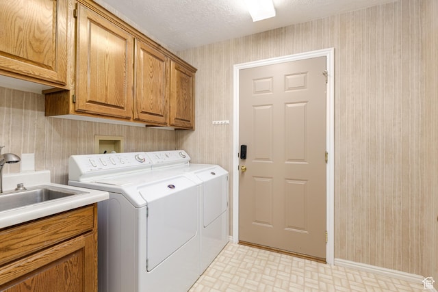 washroom featuring wallpapered walls, washing machine and clothes dryer, cabinet space, a textured ceiling, and baseboards