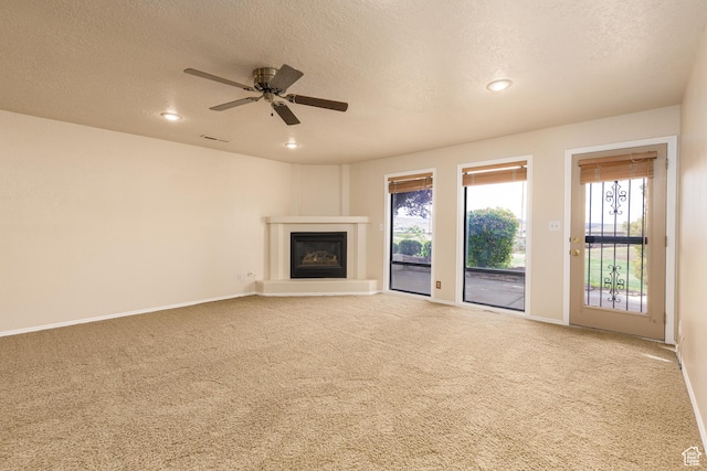 unfurnished living room with a textured ceiling, carpet, a glass covered fireplace, healthy amount of natural light, and baseboards