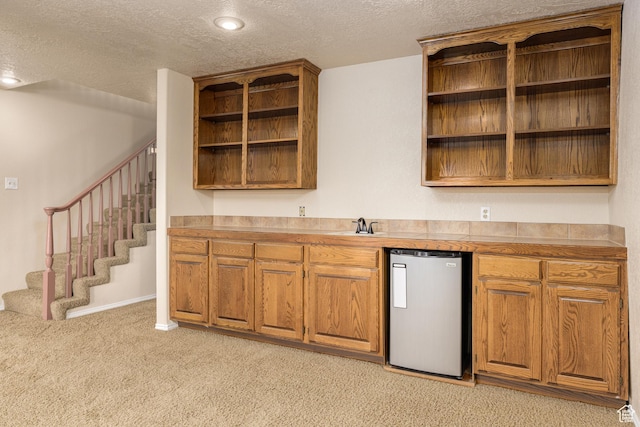 kitchen featuring open shelves, freestanding refrigerator, a textured ceiling, light colored carpet, and brown cabinetry