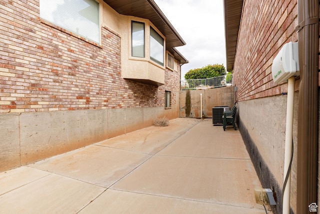view of home's exterior with central AC, brick siding, a patio, fence, and stucco siding