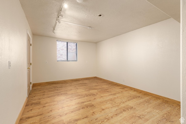 unfurnished room with light wood-style floors, a textured ceiling, track lighting, and baseboards