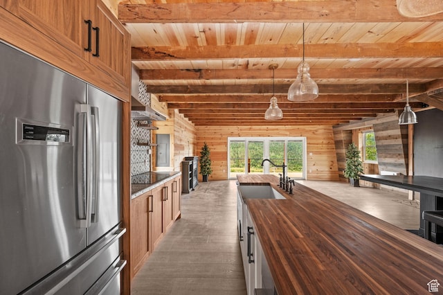kitchen featuring stainless steel fridge with ice dispenser, butcher block counters, wooden ceiling, a sink, and wood walls