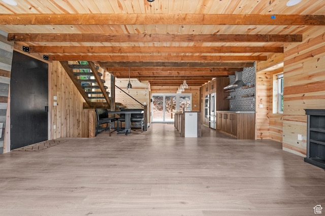 unfurnished living room featuring wood walls, wood ceiling, wood finished floors, beam ceiling, and stairs