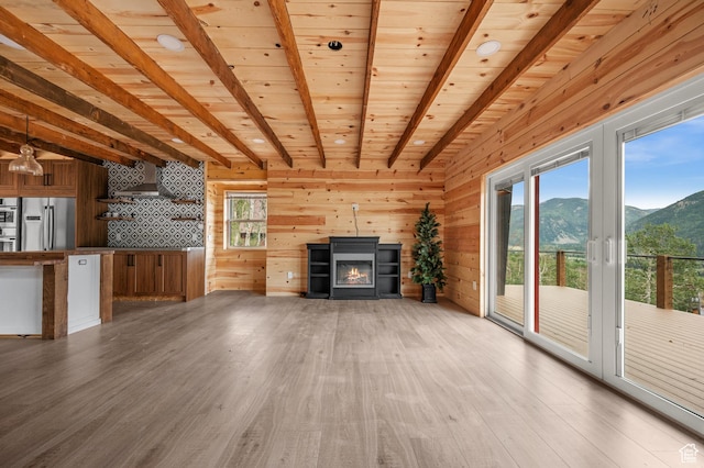 unfurnished living room featuring a mountain view, beam ceiling, light wood-style floors, a glass covered fireplace, and wood ceiling
