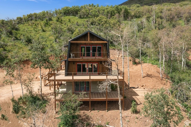 back of house with a balcony and a view of trees